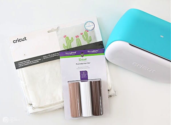 Cricut Joy cutting machine with supplies for making iron-on design on canvas pouch.